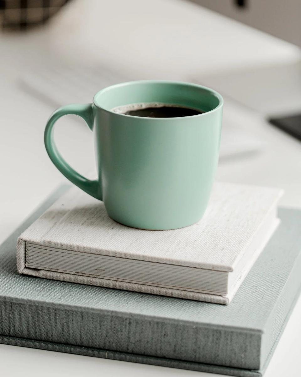 Mint stoneware mug of black coffee on a stack of linen books